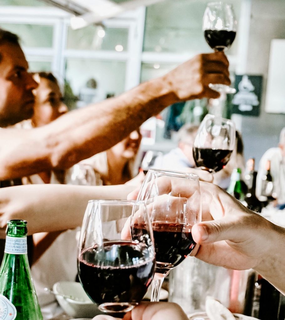 Celebre con amigos durante una reunión informal en el interior, levantando copas de vino tinto para brindar.